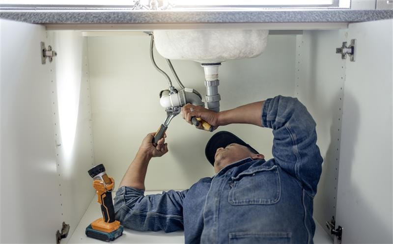 Plumber repairing pipes beneath a bathroom sink in Cocoa