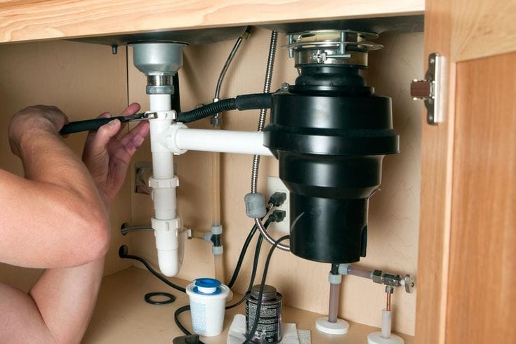 Plumber installing a garbage disposal beneath a kitchen sink in Cocoa