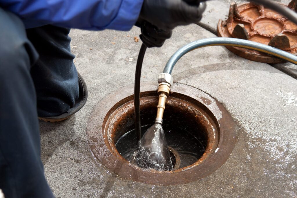 Plumber hydro jetting a sewer line through a manhole in Cocoa