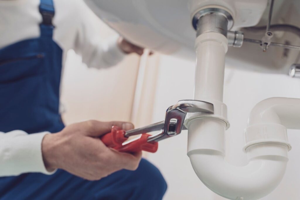 Plumber repairing a white drain pipe beneath a sink in Cocoa