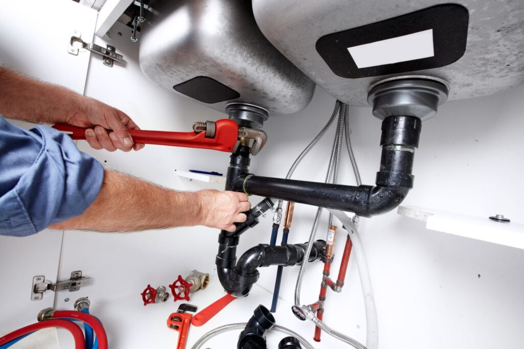 Plumber repairing drain pipes beneath a kitchen sink in Cocoa